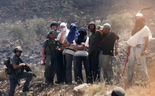 مستوطنون إسرائيليون ملثمون من شبيبة التلال ويقف إلى جانبهم جنود من جيش الاحتلال الإسرائيلي، الضفة الغربية المحتلة